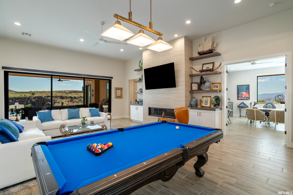 Playroom with tile walls, light hardwood / wood-style floors, a tiled fireplace, and pool table