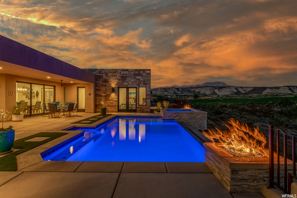 Pool at dusk with a patio, an in ground hot tub, a fire pit, and a mountain view