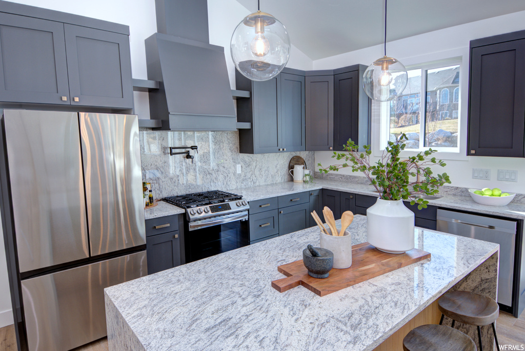 Kitchen with hanging light fixtures, appliances with stainless steel finishes, light stone countertops, a breakfast bar, and tasteful backsplash