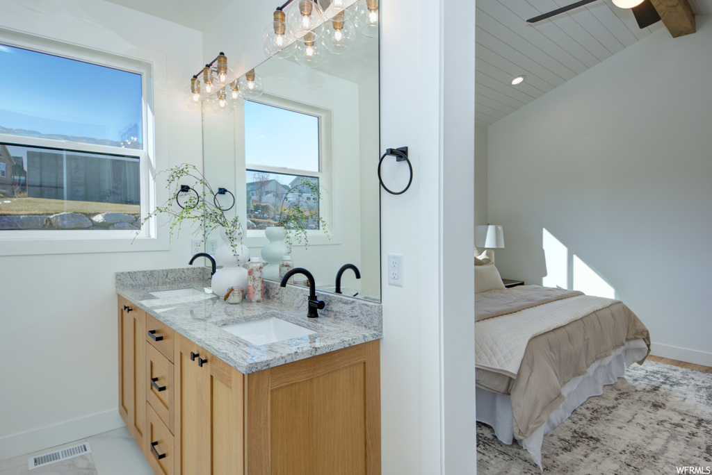 Bathroom with lofted ceiling with beams, double sink vanity, and ceiling fan with notable chandelier