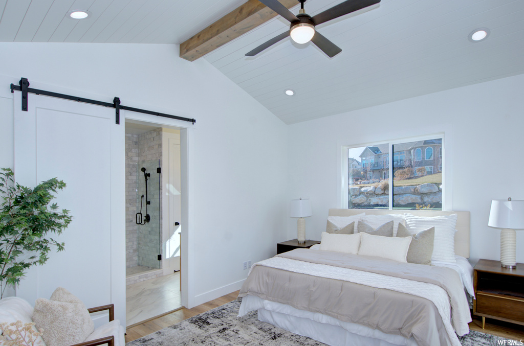Tiled bedroom featuring lofted ceiling with beams, ensuite bathroom, ceiling fan, and a barn door