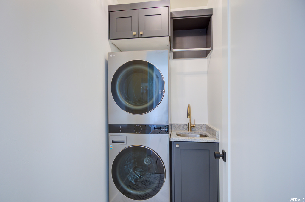 Washroom with cabinets, sink, and stacked washer and dryer