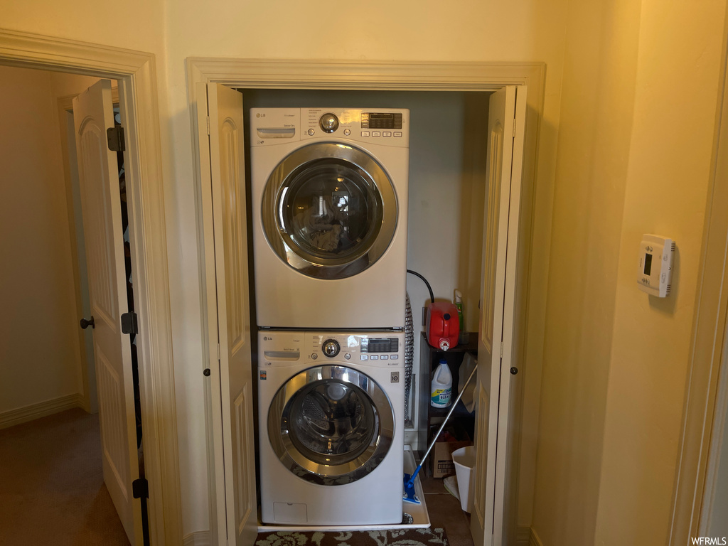Clothes washing area with dark carpet and stacked washer and dryer