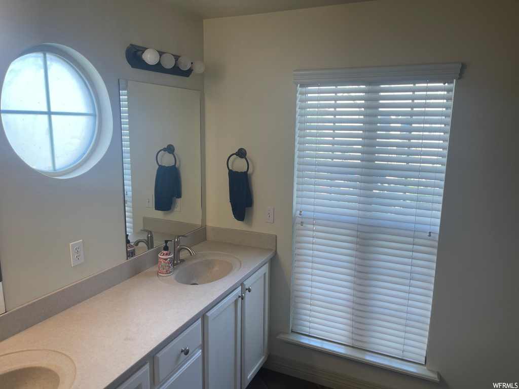 Bathroom featuring a healthy amount of sunlight, dual sinks, and vanity with extensive cabinet space