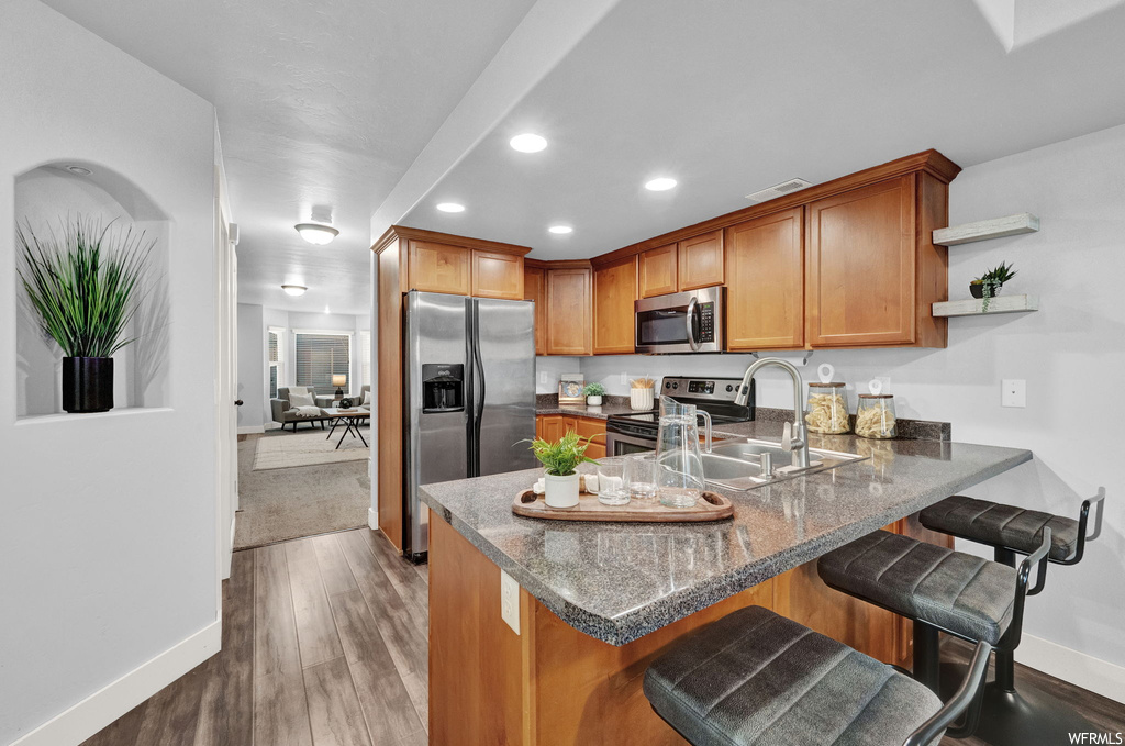Kitchen featuring sink, appliances with stainless steel finishes, dark hardwood / wood-style floors, a kitchen breakfast bar, and kitchen peninsula