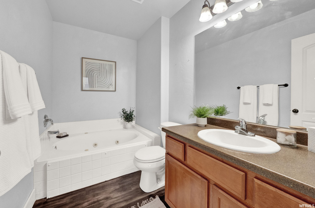 Bathroom featuring tiled bath, toilet, oversized vanity, and hardwood / wood-style flooring
