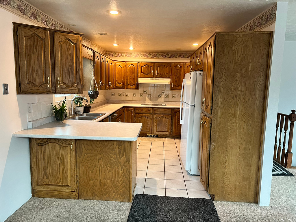 Kitchen with sink, white refrigerator, gas stovetop, backsplash, and kitchen peninsula