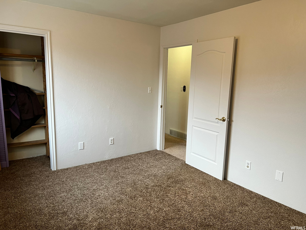 Unfurnished bedroom with a walk in closet, a closet, and dark colored carpet