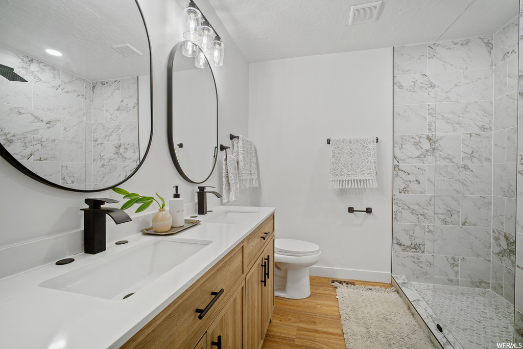 Bathroom with toilet, a textured ceiling, a tile shower, double sink vanity, and hardwood / wood-style floors