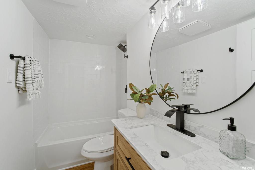 Full bathroom featuring tiled shower / bath, vanity, toilet, and a textured ceiling