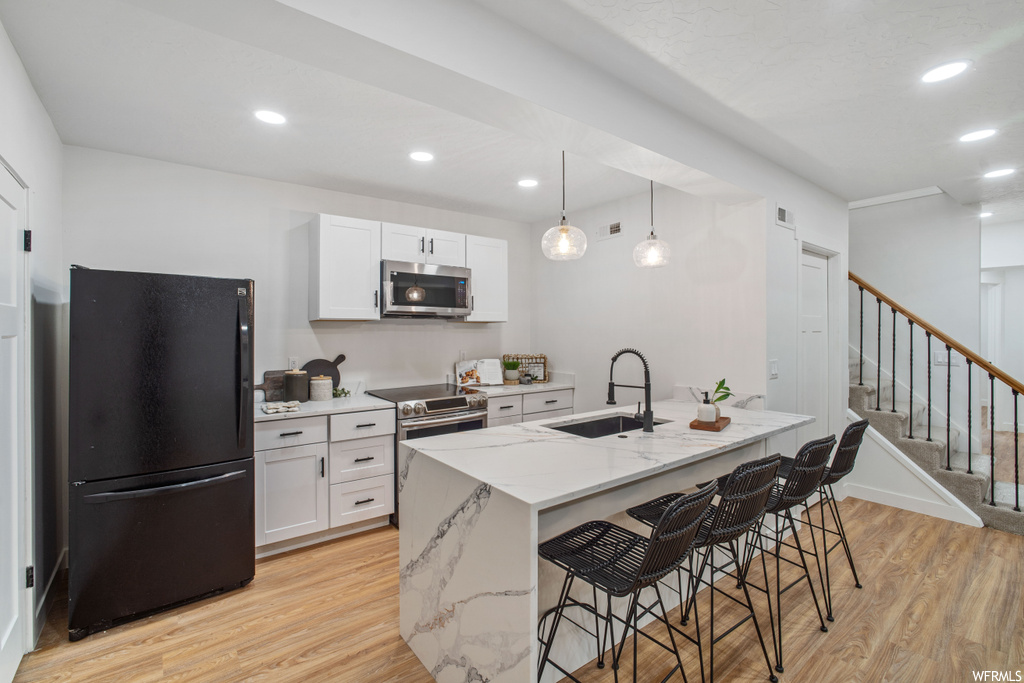 Kitchen with sink, black fridge, light hardwood / wood-style floors, decorative light fixtures, and white cabinetry