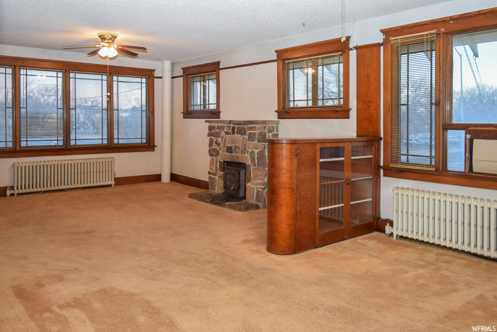 Unfurnished living room featuring light colored carpet, ceiling fan, a fireplace, and radiator
