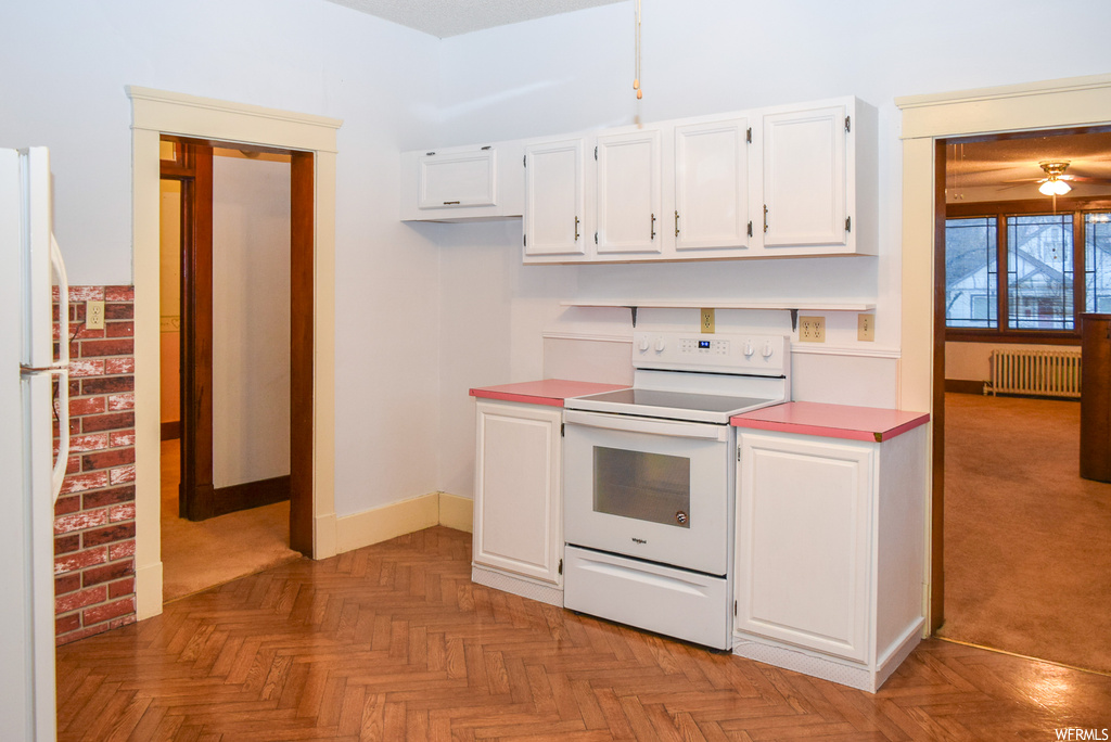 Kitchen with white appliances, light parquet floors, white cabinets, and radiator