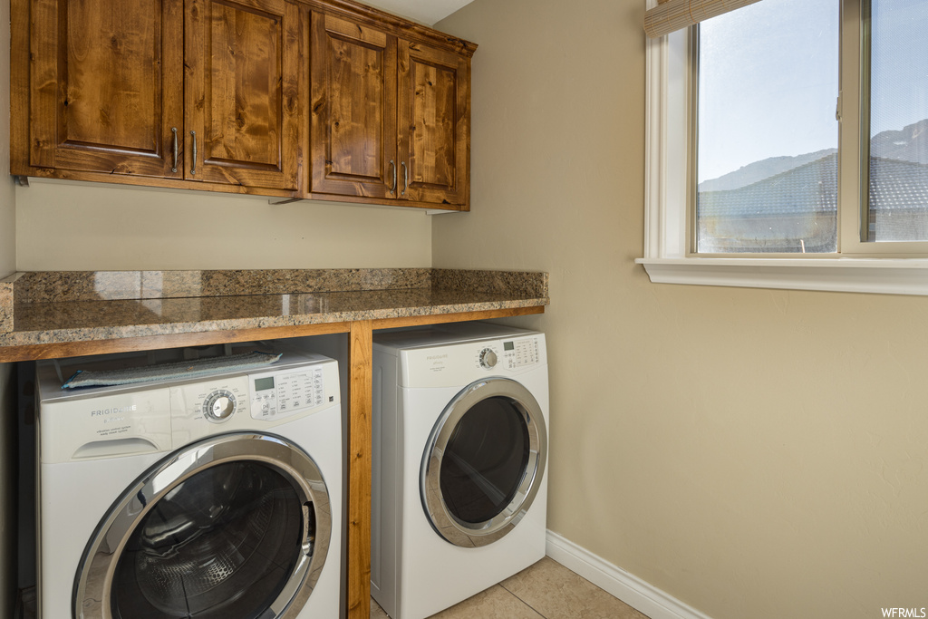 Clothes washing area with cabinets, washing machine and clothes dryer, a mountain view, and light tile floors