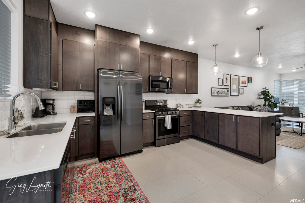 Kitchen with sink, hanging light fixtures, stainless steel appliances, kitchen peninsula, and dark brown cabinetry