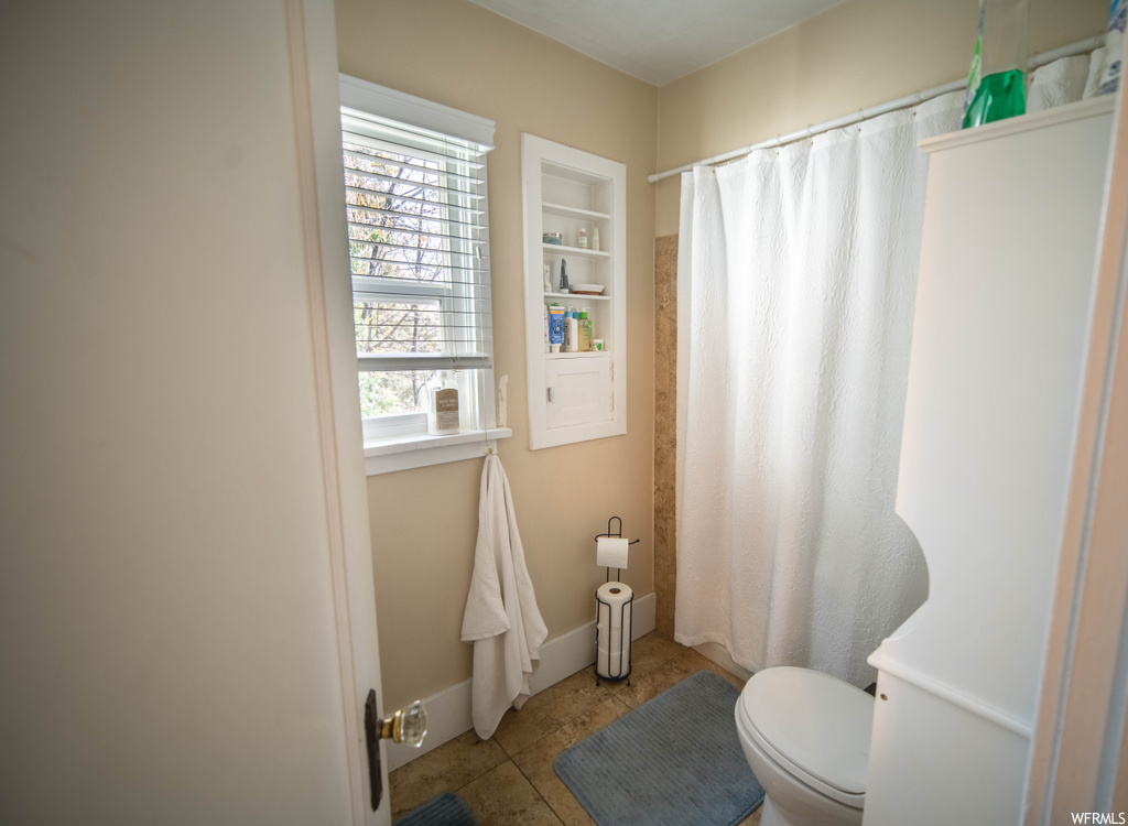 Bathroom featuring toilet, tile floors, and a healthy amount of sunlight