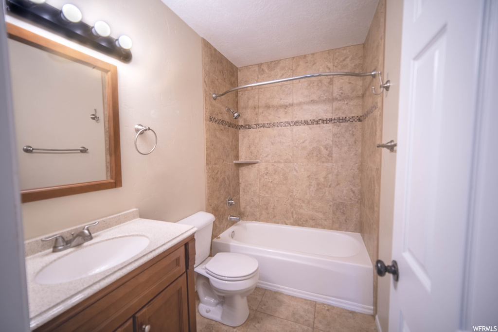 Full bathroom featuring toilet, a textured ceiling, tile flooring, tiled shower / bath, and large vanity