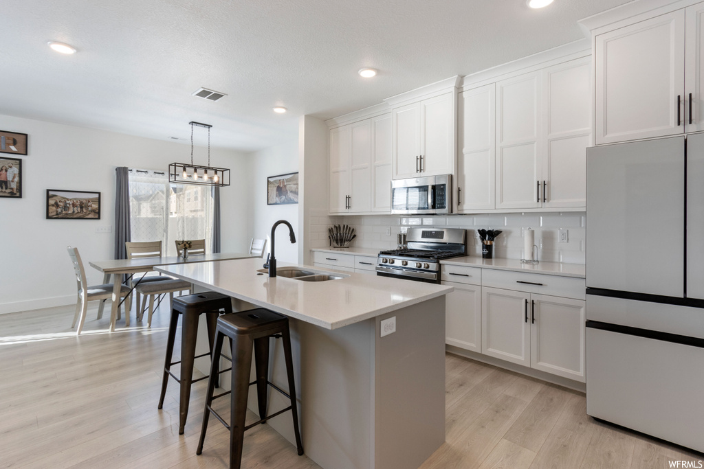 Kitchen featuring sink, hanging light fixtures, appliances with stainless steel finishes, light hardwood / wood-style floors, and white cabinetry
