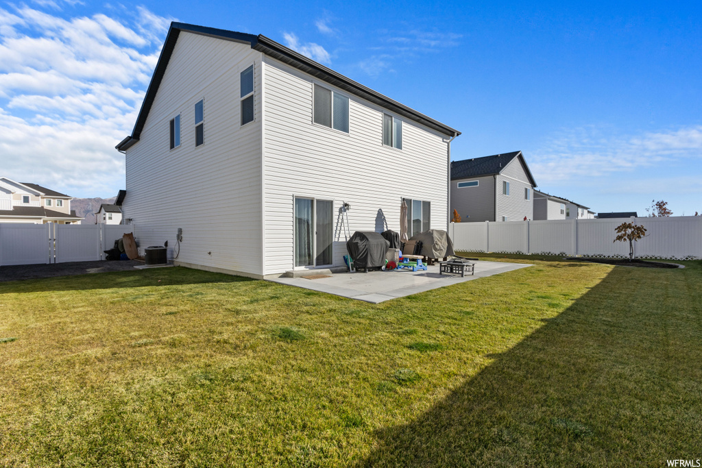 Rear view of property with a lawn, a patio, and central AC