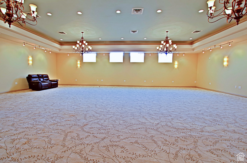 Carpeted spare room with crown molding, a tray ceiling, and a notable chandelier