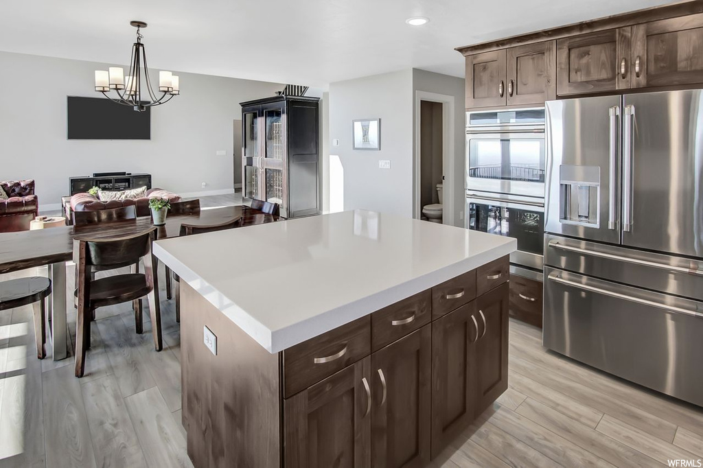 Kitchen featuring multiple ovens, hanging light fixtures, light hardwood / wood-style floors, stainless steel fridge, and a kitchen island