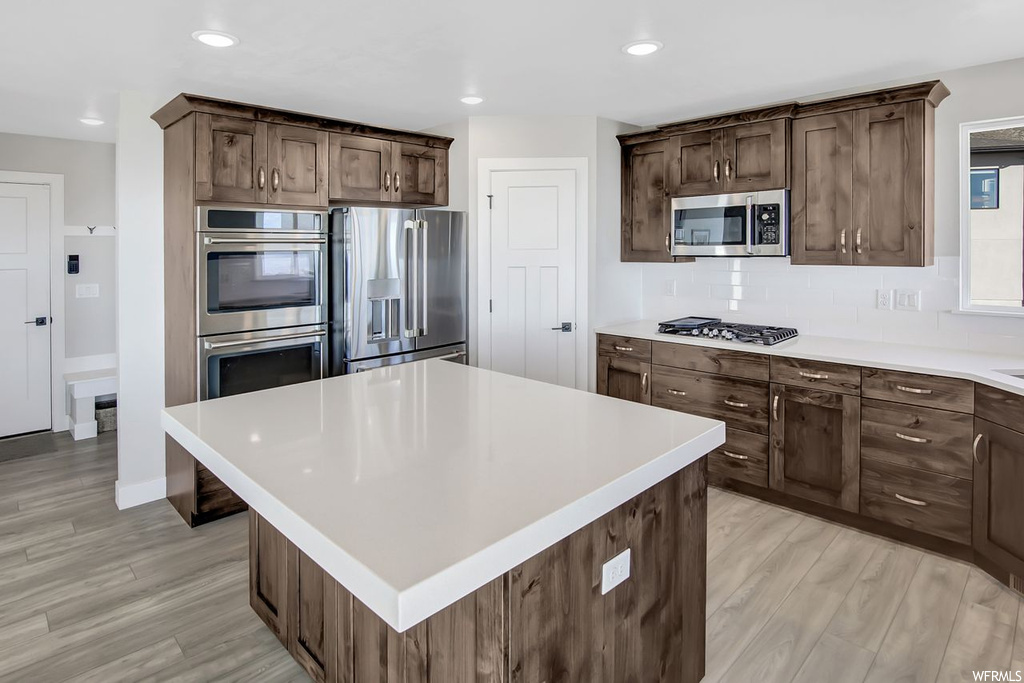 Kitchen featuring stainless steel appliances, light hardwood / wood-style floors, a center island, and backsplash
