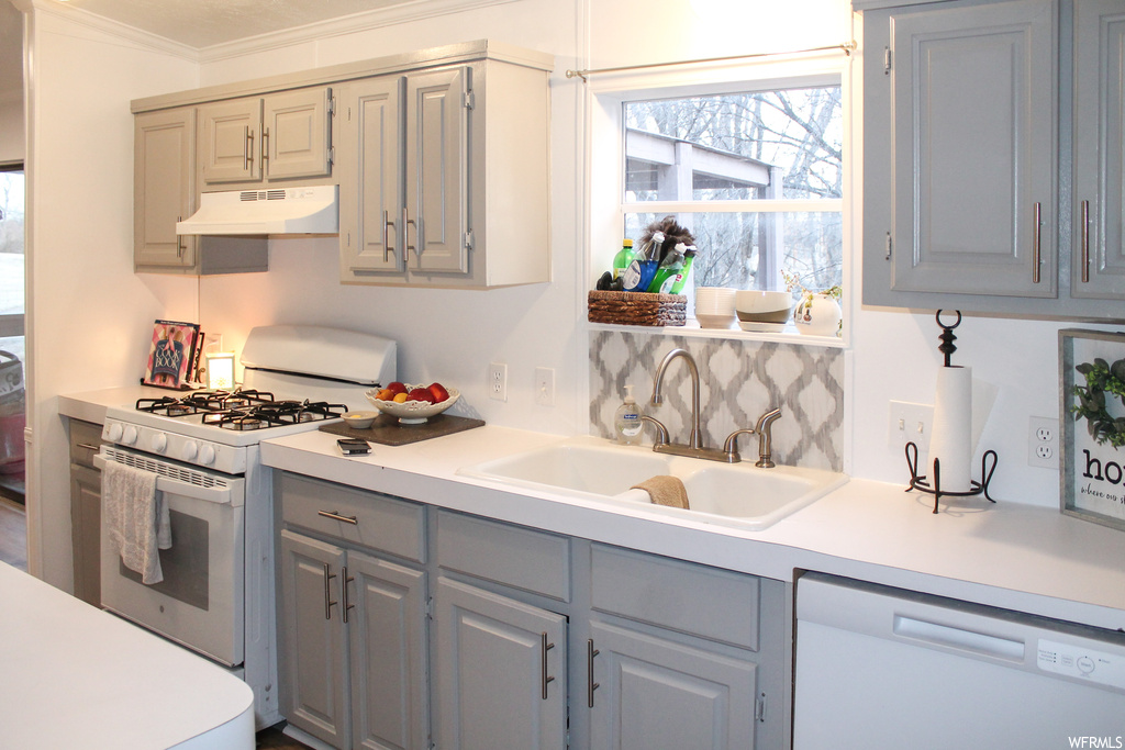 Kitchen with premium range hood, sink, gray cabinetry, white appliances, and ornamental molding
