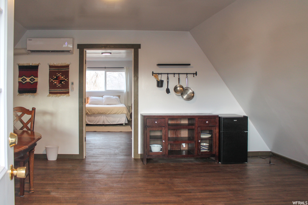 Interior space with a wall mounted air conditioner, black refrigerator, lofted ceiling, and dark hardwood / wood-style floors