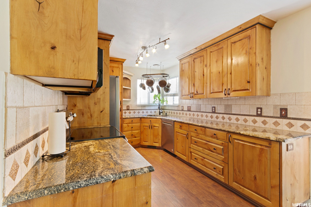 Kitchen featuring dark stone countertops, stainless steel dishwasher, rail lighting, and hardwood / wood-style flooring