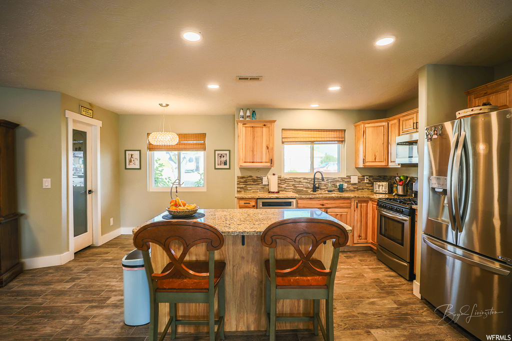 Kitchen with sink, a kitchen breakfast bar, appliances with stainless steel finishes, a kitchen island, and decorative light fixtures