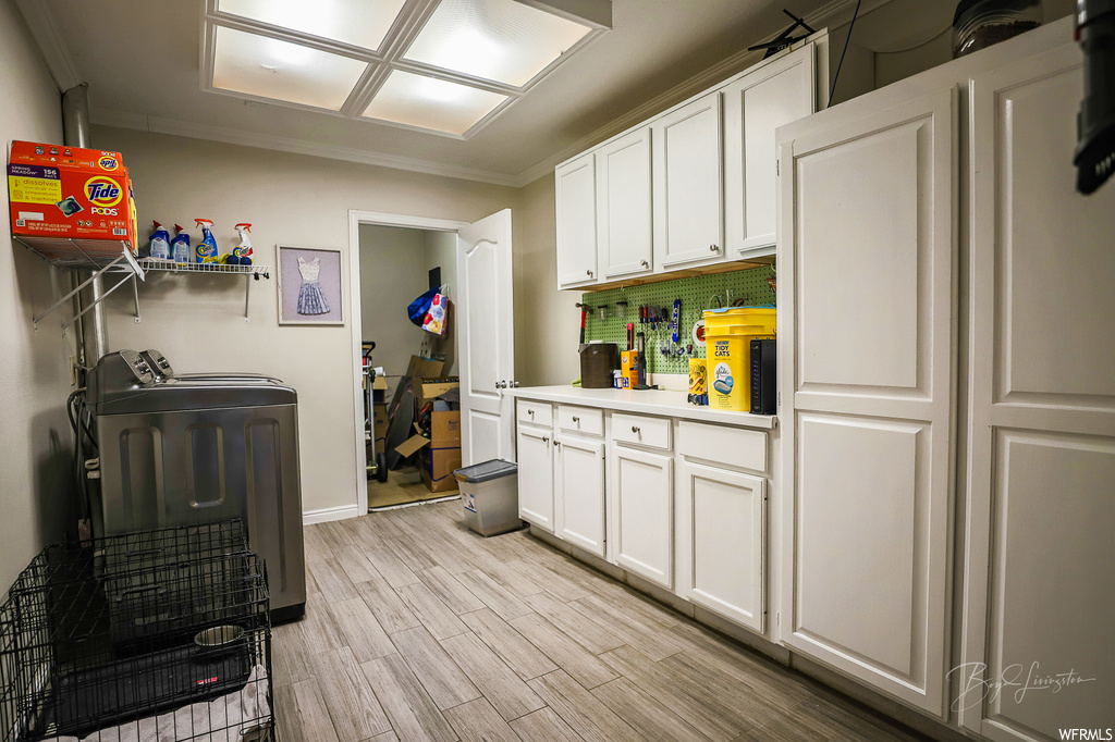 Kitchen with white cabinets, washing machine and dryer, crown molding, and light hardwood / wood-style floors