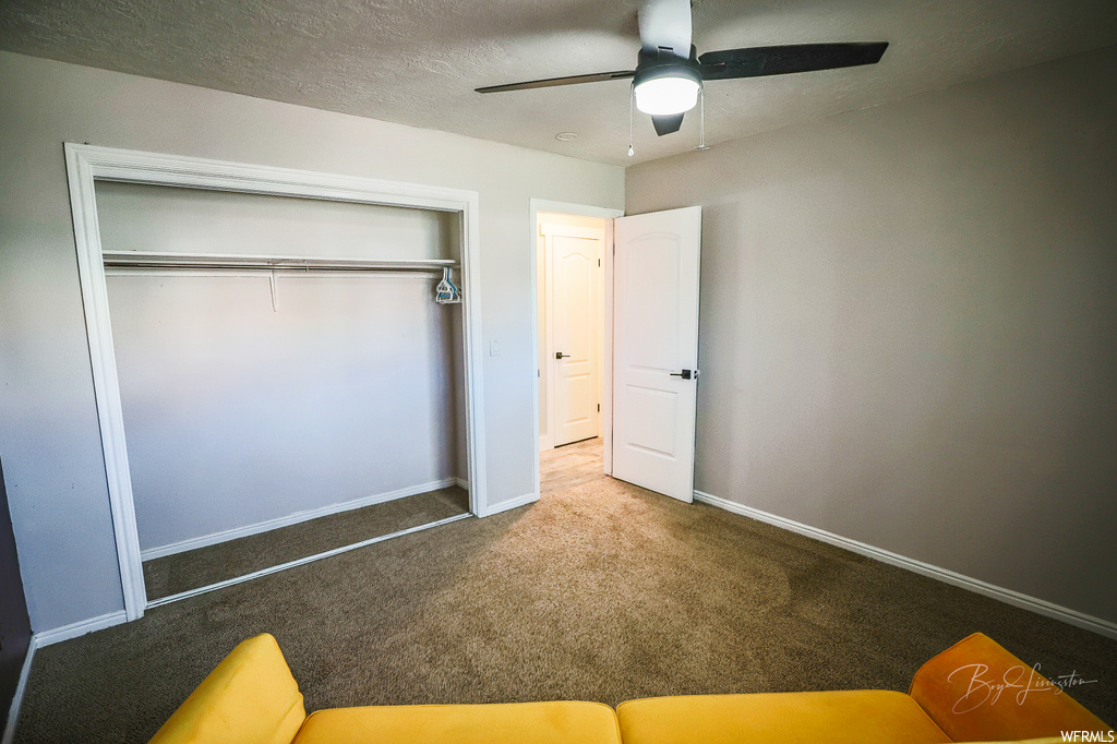 Unfurnished bedroom featuring ceiling fan, a textured ceiling, a closet, and carpet flooring