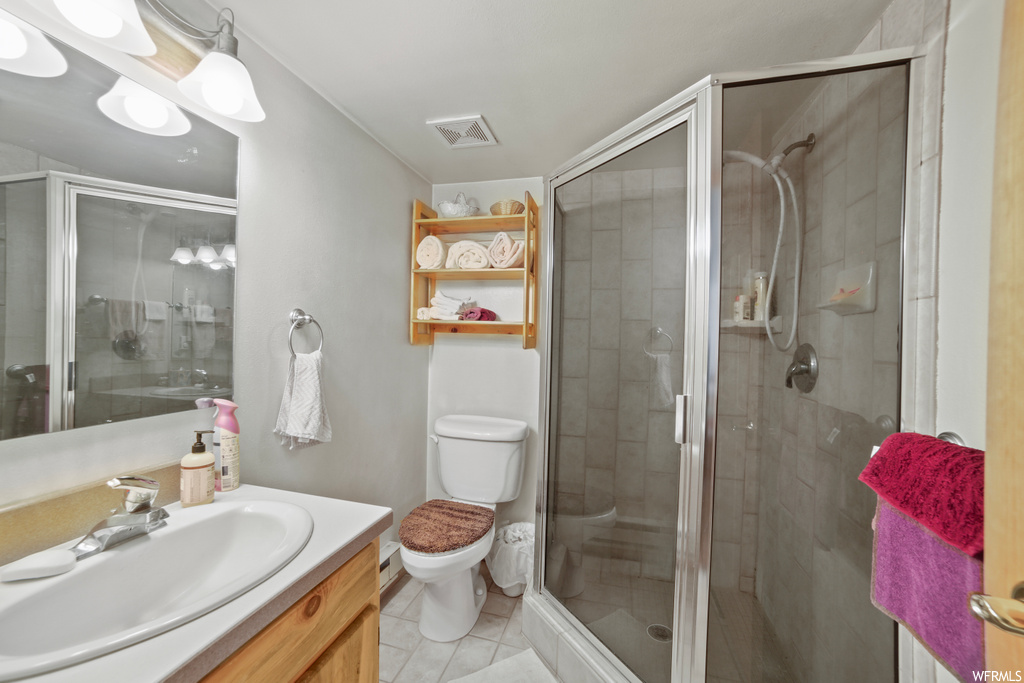 Bathroom with toilet, a shower with shower door, tile floors, and vanity