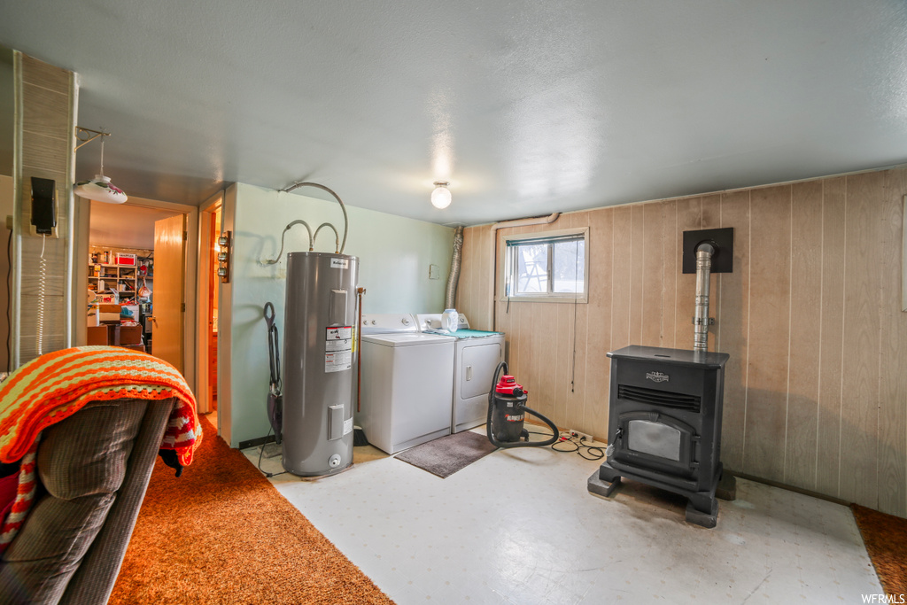 Laundry area featuring electric water heater, wood walls, washing machine and dryer, and a wood stove