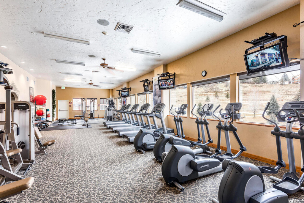 Gym with dark carpet, ceiling fan, a textured ceiling, and plenty of natural light