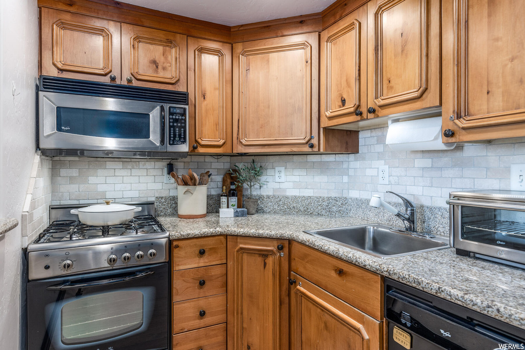 Kitchen featuring sink, range with gas cooktop, light stone countertops, dishwasher, and backsplash