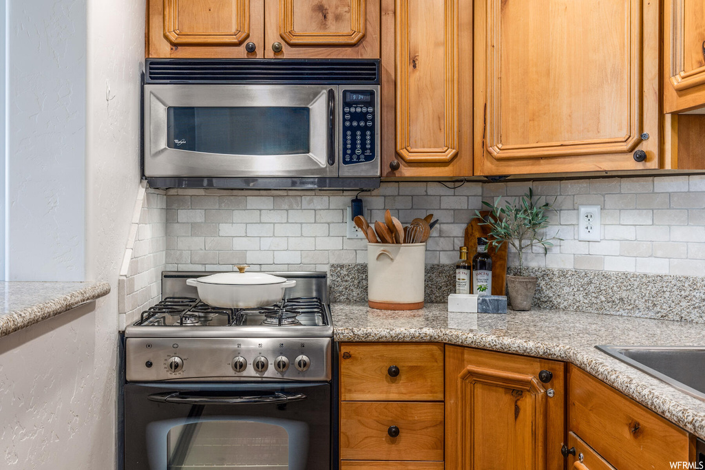 Kitchen with tasteful backsplash, light stone counters, and gas stove
