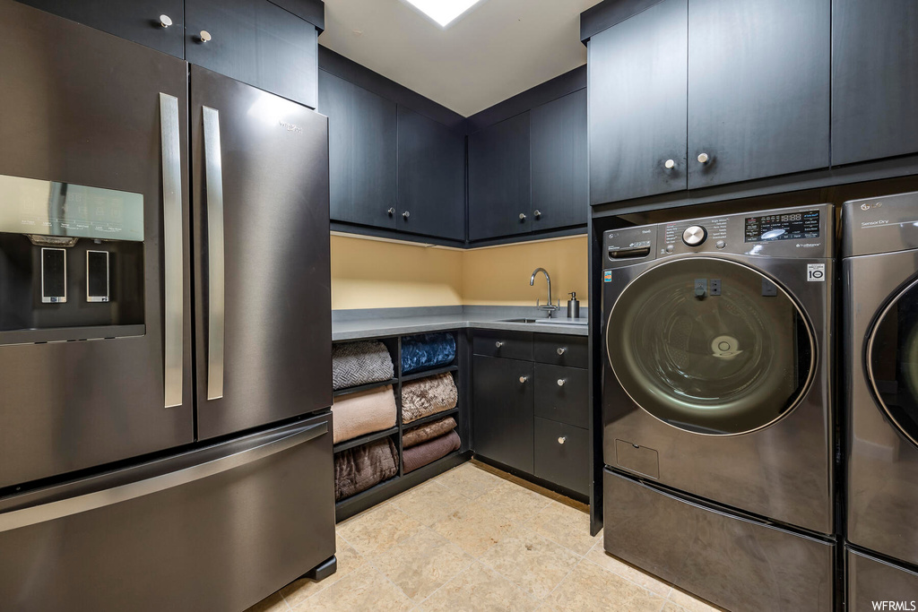 Clothes washing area with sink, separate washer and dryer, and light tile floors