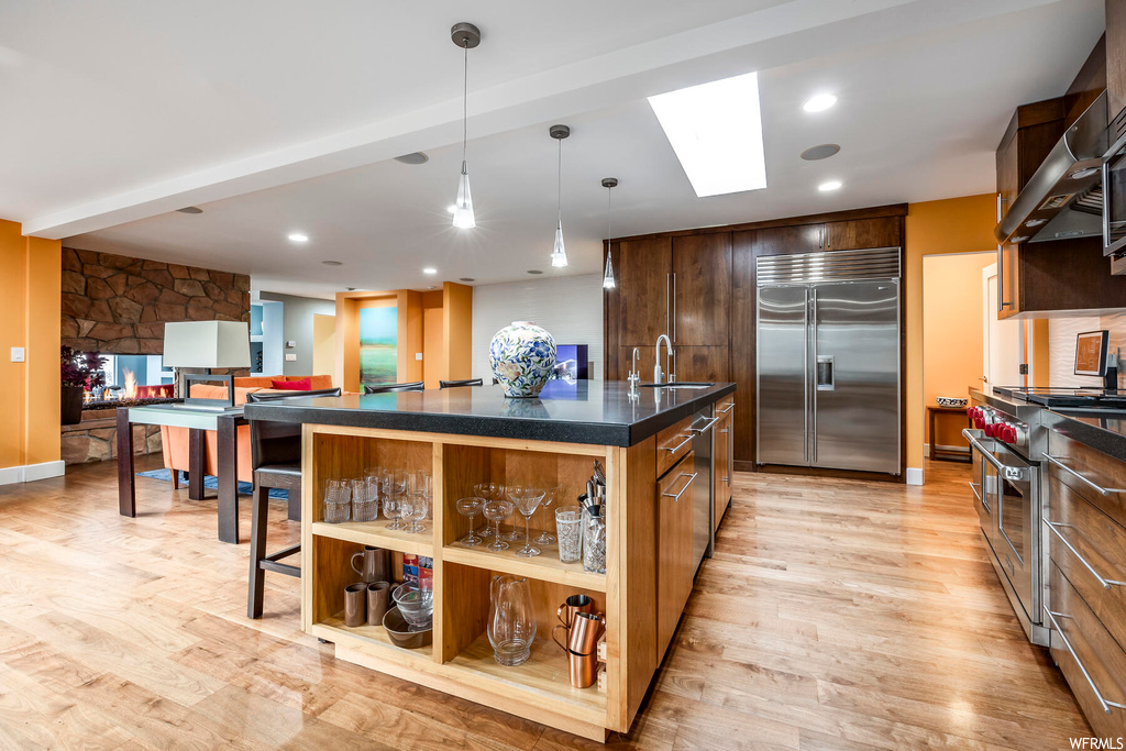 Kitchen featuring an island with sink, sink, light hardwood / wood-style flooring, high quality appliances, and a skylight