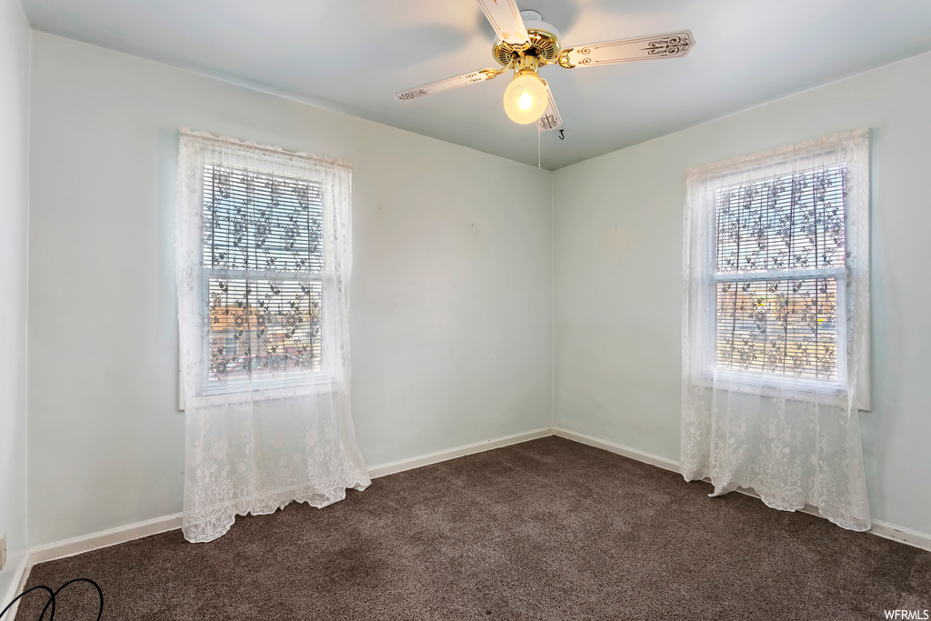Unfurnished room with dark colored carpet, ceiling fan, and plenty of natural light