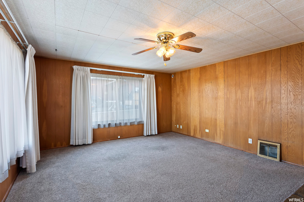 Carpeted spare room with wood walls and ceiling fan