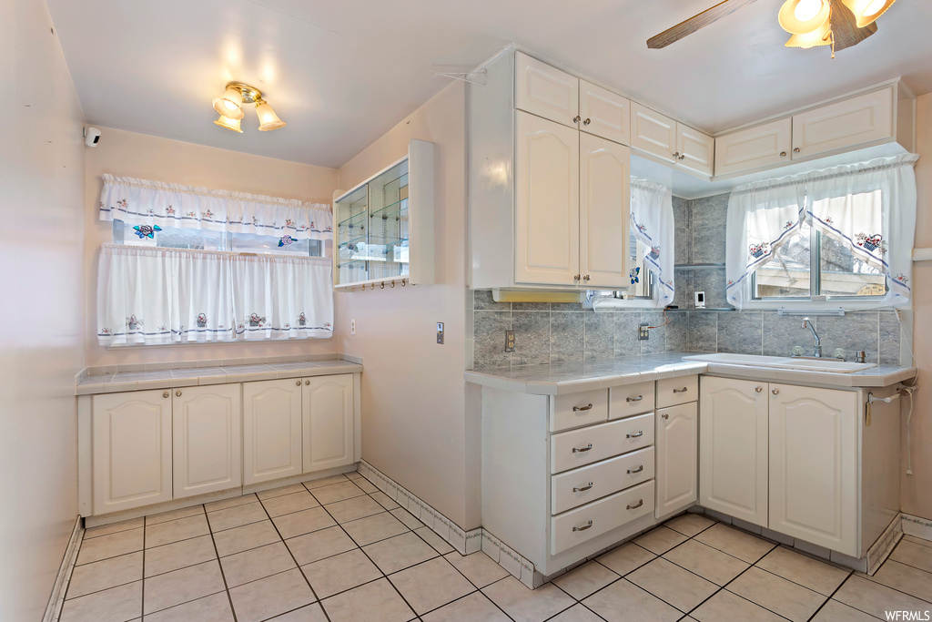 Kitchen featuring ceiling fan, white cabinets, tasteful backsplash, and light tile floors