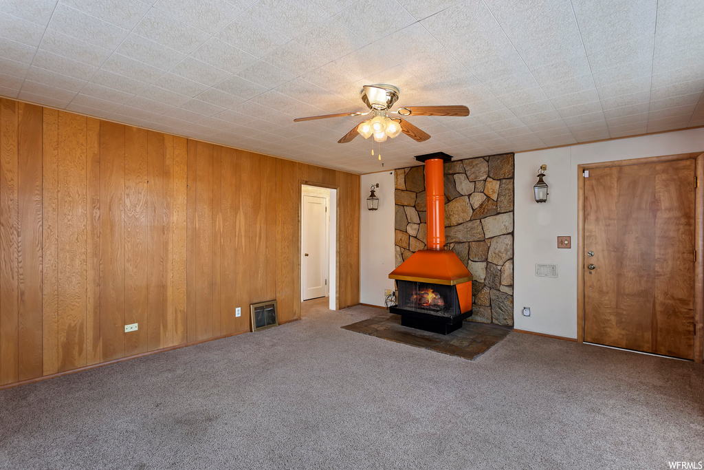 Unfurnished living room featuring wooden walls, ceiling fan, carpet, and a wood stove