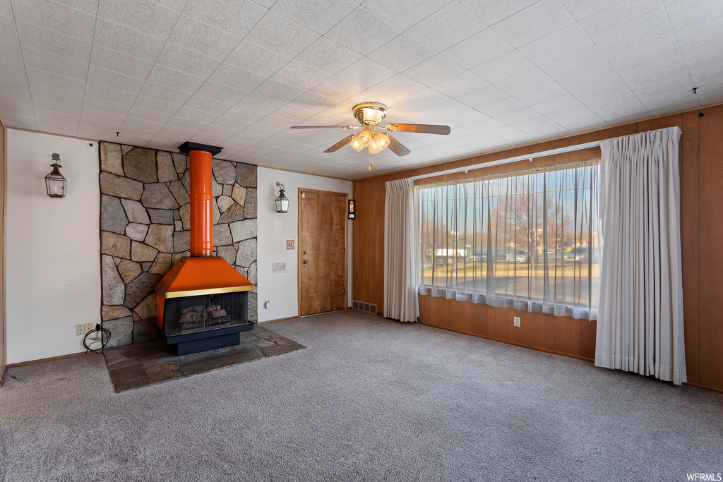 Unfurnished room featuring dark colored carpet, ceiling fan, and a wood stove