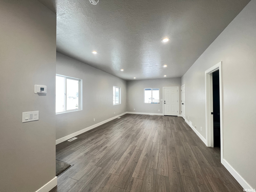 Empty room featuring a textured ceiling, plenty of natural light, and dark hardwood / wood-style flooring