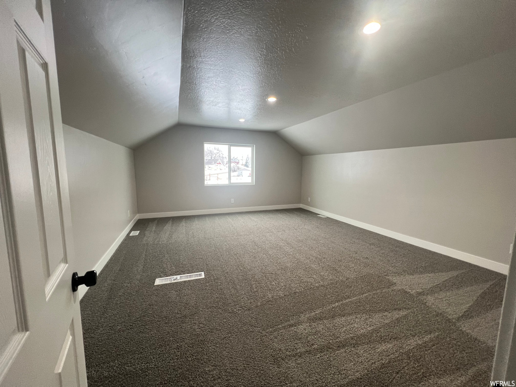 Additional living space with a textured ceiling, carpet floors, and vaulted ceiling