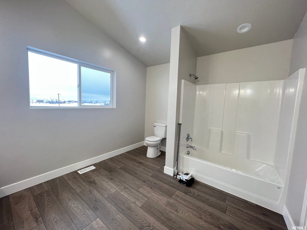 Bathroom with lofted ceiling, toilet, washtub / shower combination, and hardwood / wood-style floors