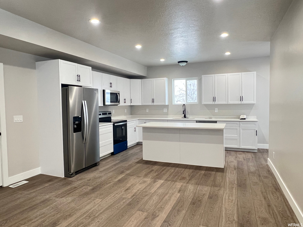 Kitchen with dark hardwood / wood-style flooring, appliances with stainless steel finishes, white cabinetry, and a center island