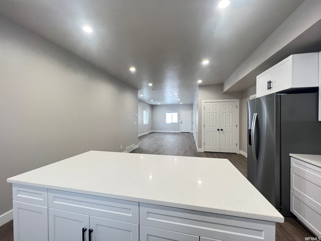 Kitchen featuring a center island, stainless steel fridge with ice dispenser, light stone counters, dark hardwood / wood-style floors, and white cabinetry