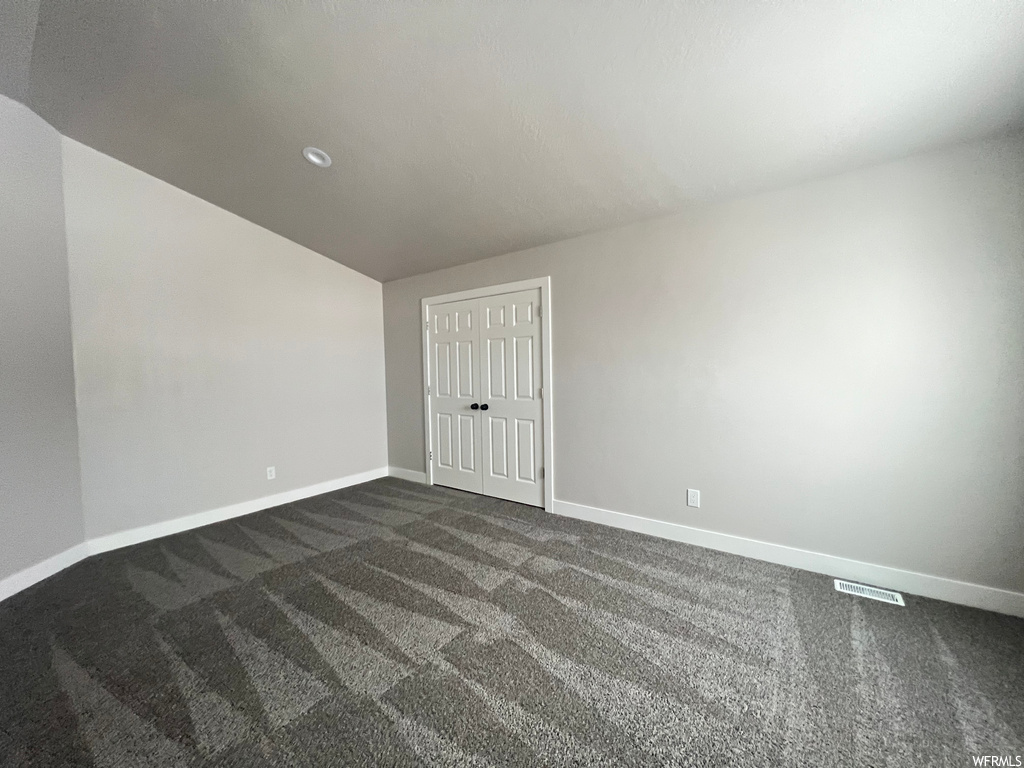 Unfurnished room with dark colored carpet and vaulted ceiling